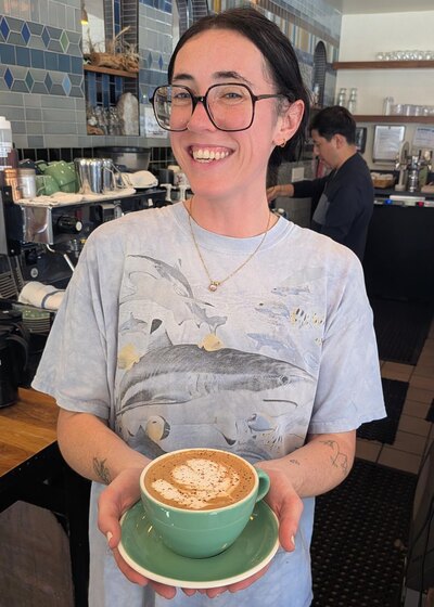 Beans: a barista at a San Francisco cafe holding a mint-green cup of mocha, latte art poured into the foam under a dusting of cocoa.